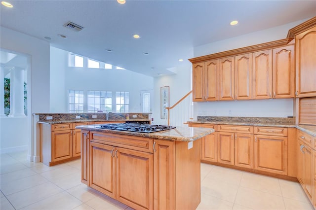 kitchen featuring a center island, kitchen peninsula, stainless steel gas cooktop, light stone countertops, and light tile patterned floors