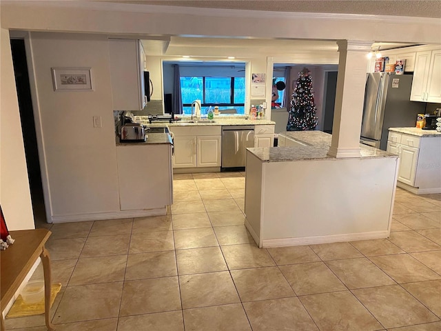 kitchen featuring appliances with stainless steel finishes, light stone counters, light tile patterned floors, white cabinets, and a center island