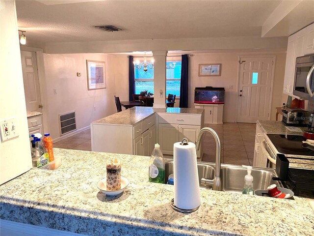 kitchen featuring sink, white cabinetry, a notable chandelier, a kitchen island, and light tile patterned flooring