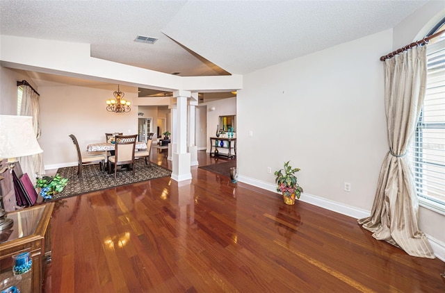 dining room with hardwood / wood-style floors, a textured ceiling, an inviting chandelier, and ornate columns