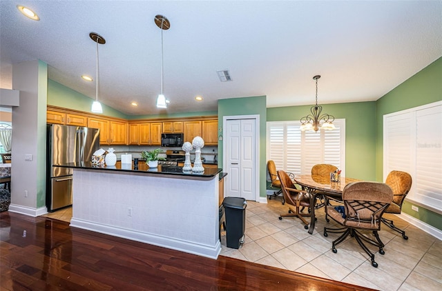 kitchen with pendant lighting, vaulted ceiling, light tile patterned floors, stainless steel appliances, and a chandelier