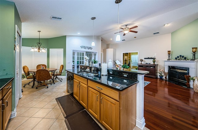 kitchen featuring sink, black dishwasher, dark stone counters, decorative light fixtures, and a kitchen island with sink