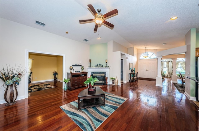 living room featuring ceiling fan, a premium fireplace, a textured ceiling, and dark wood-type flooring