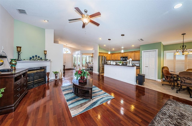 living room with ceiling fan with notable chandelier, a premium fireplace, light hardwood / wood-style flooring, and vaulted ceiling