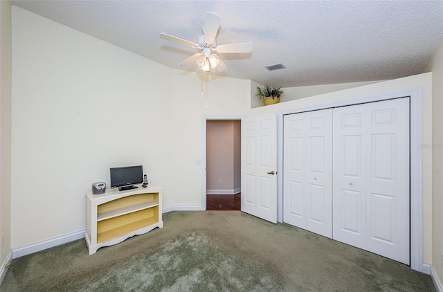 interior space with ceiling fan, a textured ceiling, lofted ceiling, a closet, and dark carpet