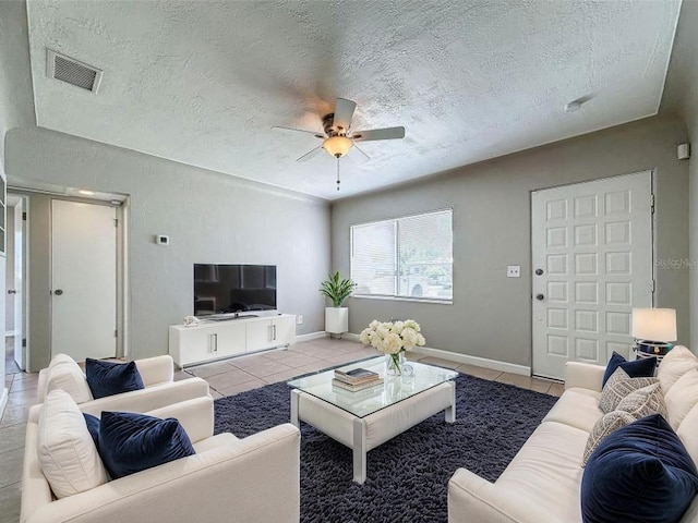 living room featuring a textured ceiling, a ceiling fan, baseboards, light tile patterned floors, and visible vents