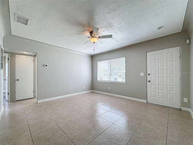 empty room with tile patterned flooring, ceiling fan, a textured ceiling, and visible vents