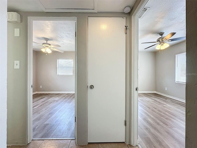 hall featuring baseboards, visible vents, a textured ceiling, and wood finished floors