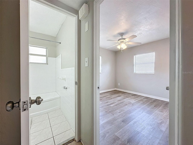 full bath with ceiling fan, a textured ceiling, baseboards, bathing tub / shower combination, and wood finished floors