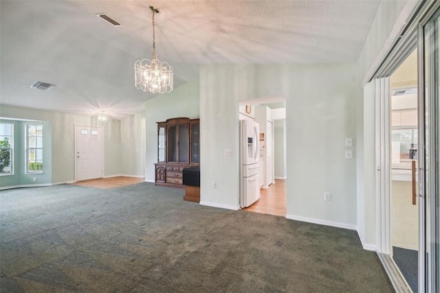 unfurnished living room with a textured ceiling, an inviting chandelier, and dark carpet