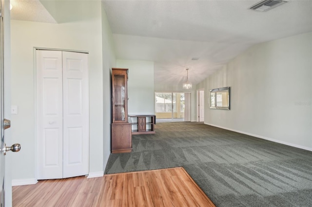 unfurnished living room featuring a textured ceiling, dark carpet, lofted ceiling, and a notable chandelier