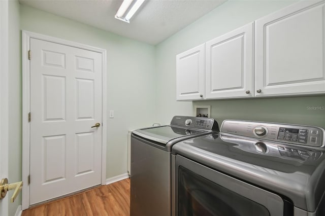 washroom with cabinets, independent washer and dryer, light wood-type flooring, and a textured ceiling