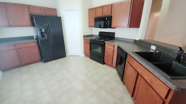 kitchen with dark countertops, black appliances, light floors, and a sink