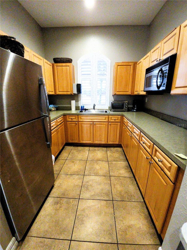 kitchen with a toaster, light tile patterned floors, freestanding refrigerator, a sink, and black microwave