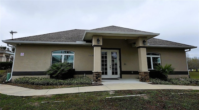 view of front facade featuring french doors, a shingled roof, and stucco siding