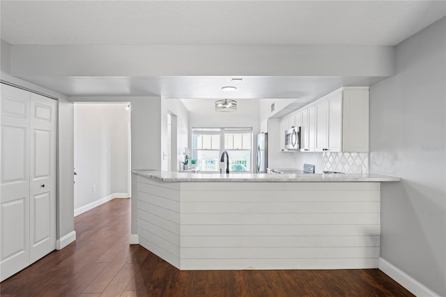 kitchen featuring kitchen peninsula, appliances with stainless steel finishes, decorative backsplash, dark wood-type flooring, and white cabinets