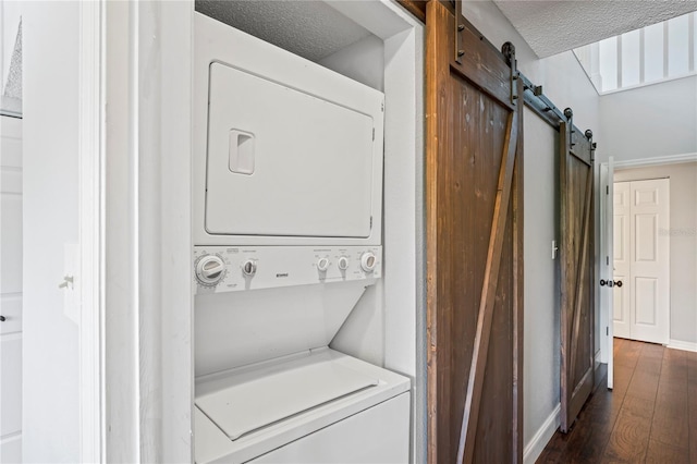 clothes washing area with a textured ceiling, dark hardwood / wood-style floors, a barn door, and stacked washer and dryer