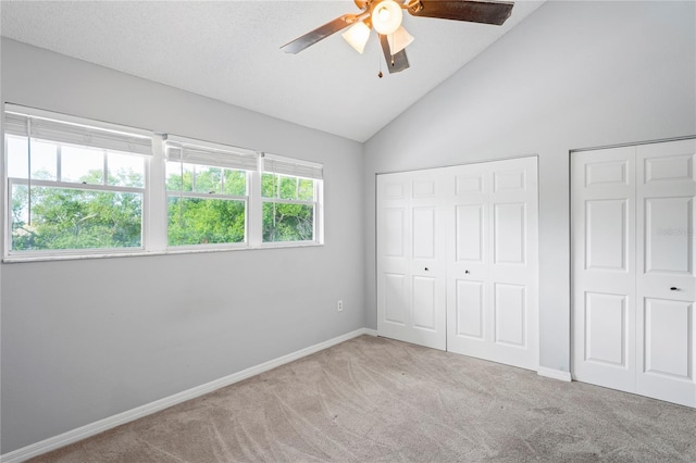 unfurnished bedroom featuring light colored carpet, high vaulted ceiling, ceiling fan, and multiple closets