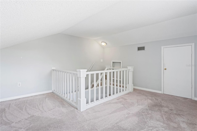 additional living space featuring a textured ceiling, light carpet, and vaulted ceiling