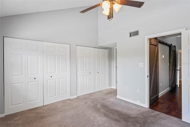 unfurnished bedroom with a barn door, ceiling fan, two closets, and dark colored carpet