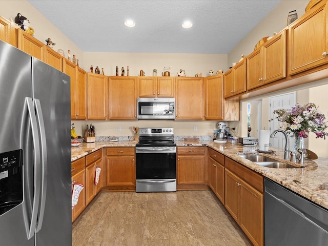 kitchen with light stone countertops, a textured ceiling, stainless steel appliances, and sink