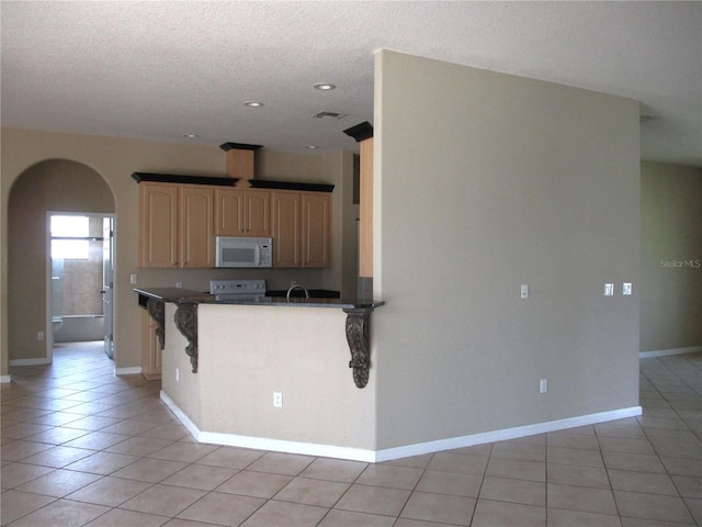 kitchen featuring light tile patterned floors, light brown cabinetry, white appliances, and kitchen peninsula