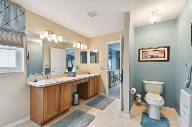 bathroom with a textured ceiling, tile flooring, toilet, and double sink vanity