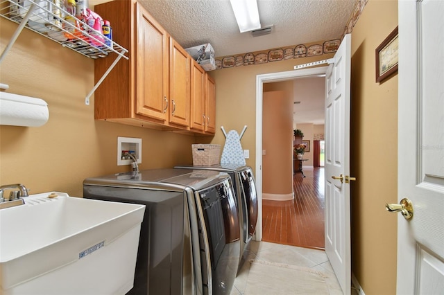 clothes washing area with cabinets, a textured ceiling, washer and clothes dryer, sink, and light tile floors