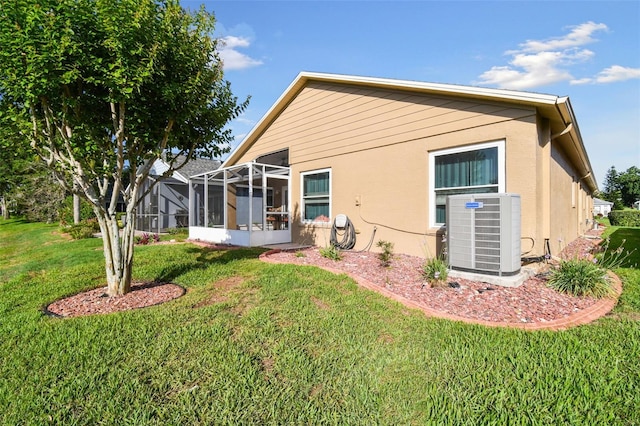 rear view of house featuring a lanai, central AC unit, and a lawn