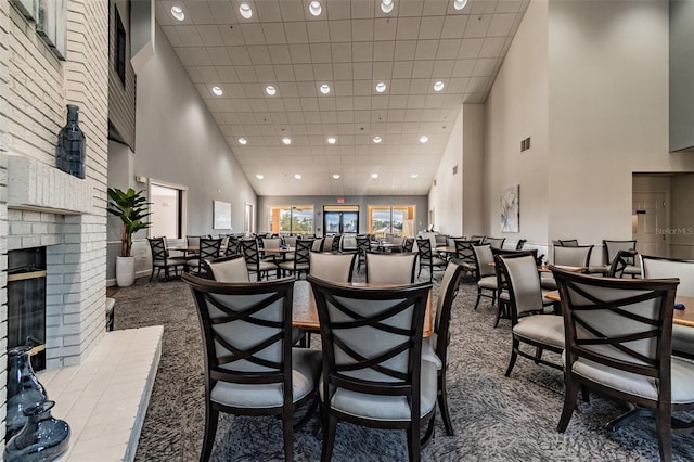 carpeted dining space with brick wall, a towering ceiling, a fireplace, and a paneled ceiling