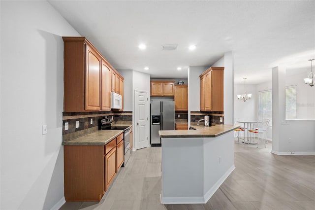 kitchen featuring kitchen peninsula, appliances with stainless steel finishes, backsplash, pendant lighting, and a chandelier