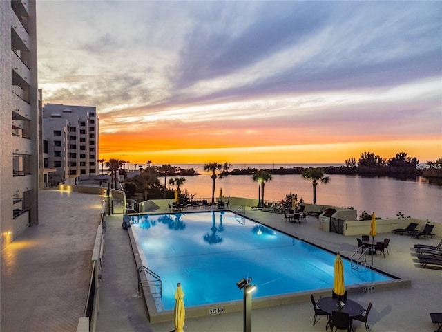 pool at dusk featuring a patio area and a water view