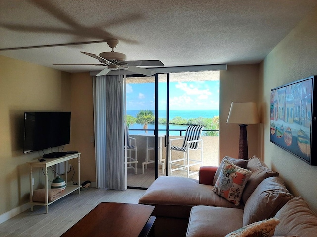 living room with ceiling fan, a water view, light hardwood / wood-style floors, and a textured ceiling