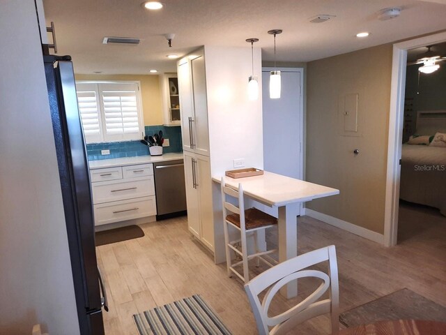 kitchen featuring hanging light fixtures, stainless steel appliances, decorative backsplash, white cabinets, and light wood-type flooring