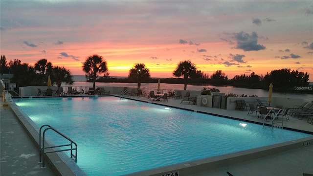 pool at dusk with a patio area and a water view