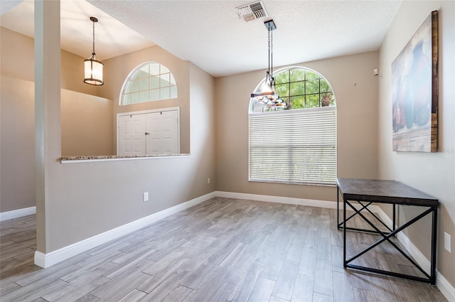 unfurnished dining area featuring light wood-type flooring and a textured ceiling