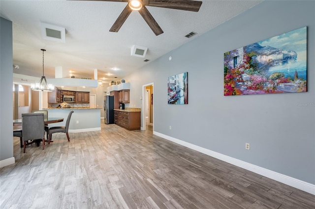 living room featuring ceiling fan with notable chandelier, a textured ceiling, and light hardwood / wood-style flooring