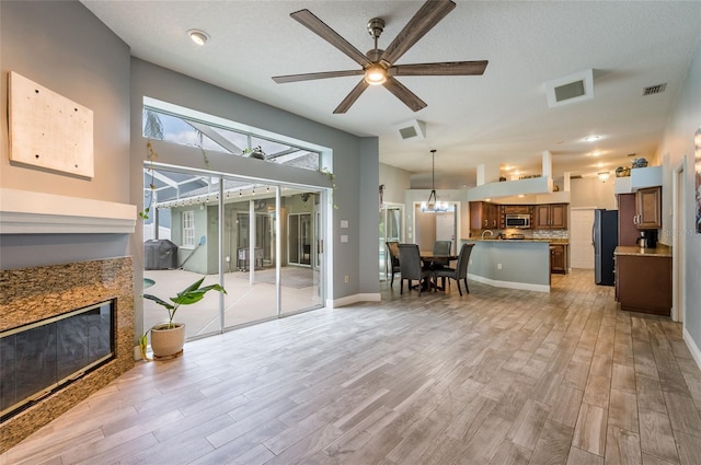 living room with a textured ceiling, ceiling fan with notable chandelier, and light hardwood / wood-style flooring