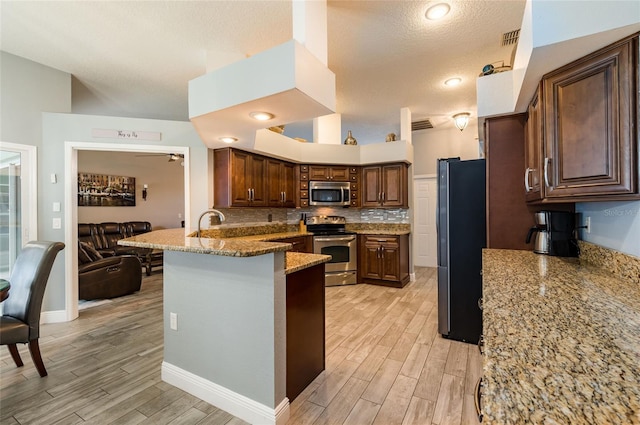 kitchen with stainless steel appliances, light stone counters, kitchen peninsula, light hardwood / wood-style floors, and decorative backsplash