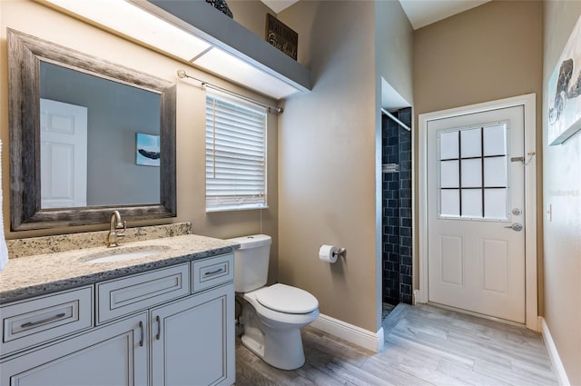 bathroom with toilet, hardwood / wood-style floors, vanity, and a tile shower