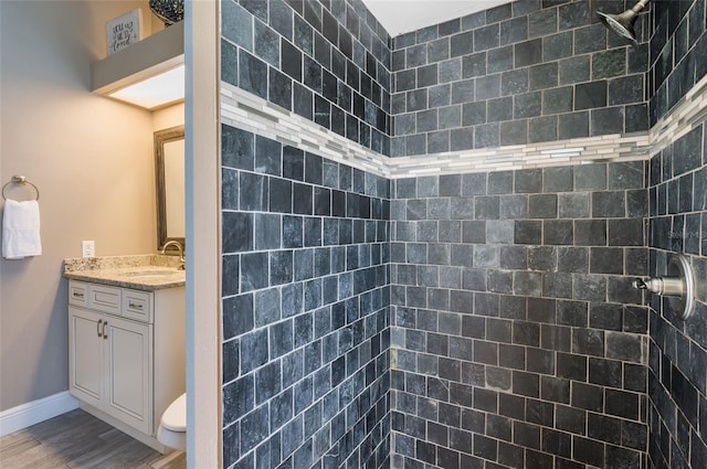 bathroom featuring tiled shower, hardwood / wood-style floors, vanity, and toilet