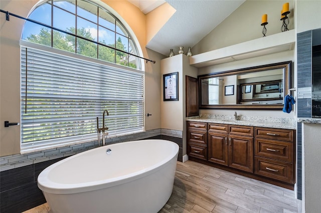 bathroom with vanity, plenty of natural light, a bathtub, and lofted ceiling