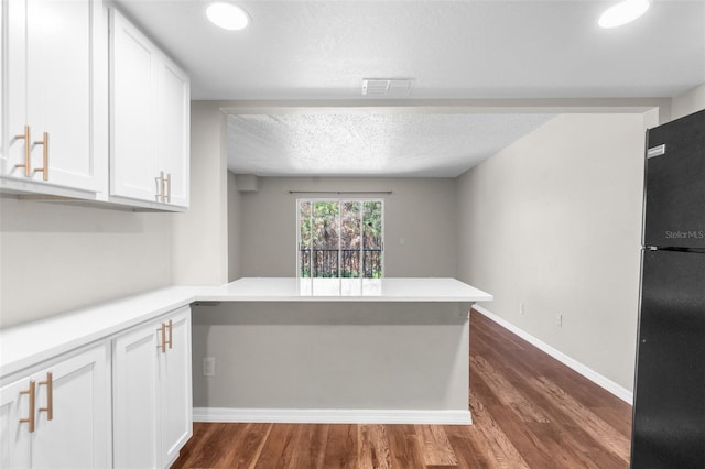 kitchen featuring kitchen peninsula, black fridge, a textured ceiling, white cabinets, and dark hardwood / wood-style floors