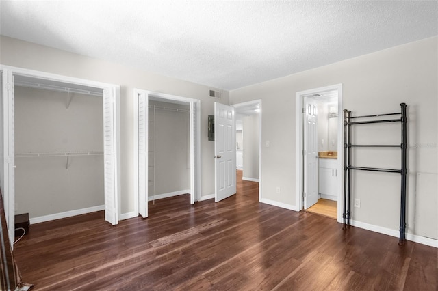 unfurnished bedroom with a textured ceiling, two closets, ensuite bath, and dark hardwood / wood-style floors