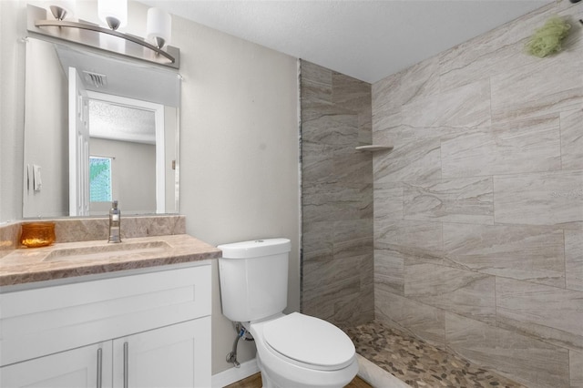 bathroom featuring vanity, toilet, a textured ceiling, and a tile shower