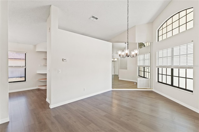 unfurnished dining area with dark wood-type flooring, a textured ceiling, plenty of natural light, and a chandelier