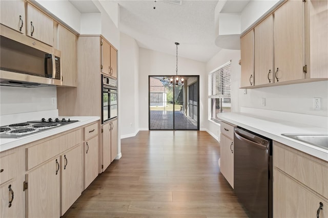 kitchen featuring light brown cabinetry, decorative light fixtures, vaulted ceiling, light hardwood / wood-style flooring, and appliances with stainless steel finishes