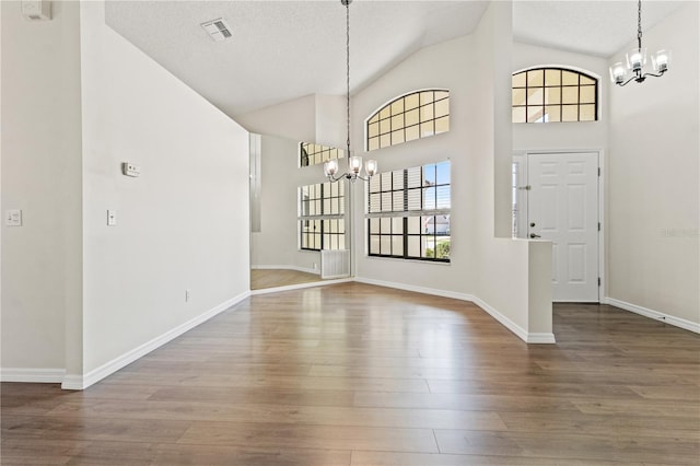 foyer entrance with wood-type flooring, high vaulted ceiling, a textured ceiling, and an inviting chandelier