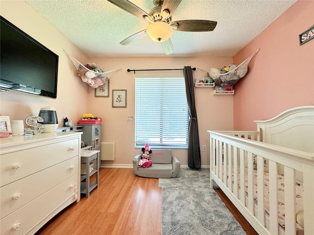 bedroom featuring ceiling fan, wood-type flooring, a textured ceiling, and a crib