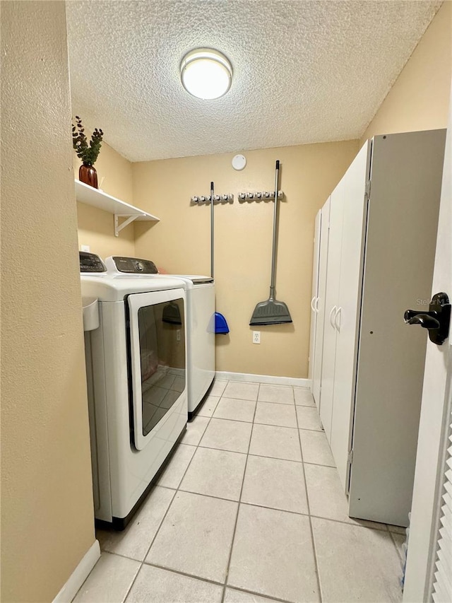 clothes washing area featuring a textured ceiling, separate washer and dryer, and light tile patterned flooring